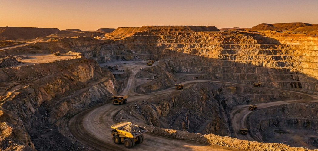 Gold mining stocks: open-pit gold mine with haul trucks at golden hour