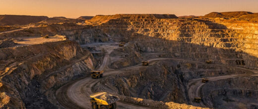 Gold mining stocks: open-pit gold mine with haul trucks at golden hour